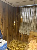 Full vertical view of the floor-to-ceiling pole light fixture with two lit amber textured glass shades in a room with wood paneling and brown carpet.