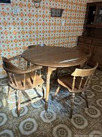 Round wood dining table with visible wear on surface, two chairs positioned around it, showing overall vintage condition.