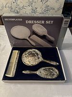 Photo of never used silverplated dresser set with hand mirror, hairbrush, and comb in original box