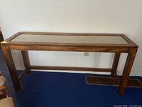 Full view of rectangular wooden sofa table with cane inset top on blue carpet against white wall.