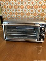 Front view of stainless steel Hamilton Beach toaster oven showing glass door and control panel with knobs