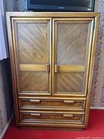 Front view of wooden wardrobe with two closed doors and two bottom drawers, showing diagonal carved panel design and wooden handles.