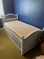 White wicker twin bed with trundle and mattress in bedroom with blue walls