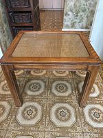 Front-facing photo of wood side table showing glass top and woven cane surface, placed on patterned tile floor.