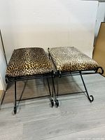 Photo of two animal print cushioned stools with black wrought iron bases, shown side by side from the front and at an angle