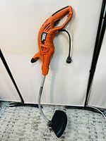 Full view of the orange and black Black & Decker corded weed eater showing handle, power cord, aluminum shaft, and protective guard.