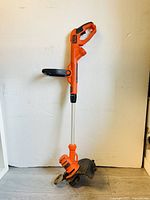 Full view of Black & Decker orange and black corded electric weed eater and edger, showing handle, trigger, secondary handle, metal shaft, and safety guard.