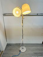 Metal floor lamp with two lampshades on a round base. The photo shows the full lamp in an upright position against a plain wall.