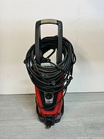 Front view full photo showing the red and black Husky power washer unit with extended power cord coiled around the handle.