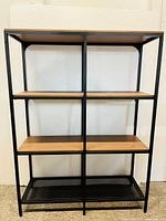 Front view of the shelving unit showing four wood shelves and metal mesh bottom shelf with black metal frame.