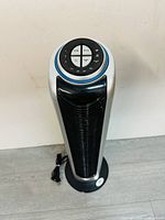 Front view of the white indoor tower fan showing circular top control panel with buttons and black vent grill