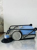 Side profile view of the Kranzle sweeper showing large side brush, wheel, and foldable handle on the floor.