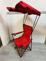Front view of red foldable lawn or beach chair with shelter canopy and cup holder on armrest