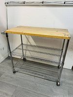 Front side view of 3-tier kitchen cart showing oak wood tabletop and three wire shelves on caster wheels.