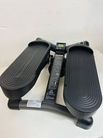 Front view of the black mini stepper showing the wide textured foot pedals and central assembly.