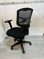 Photo of black office chair angled to show mesh back, armrests, cushioned seat, and rolling wheels
