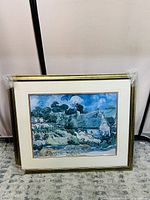 Framed landscape painting showing a cottage under swirling clouds, wrapped in protective plastic at corners.