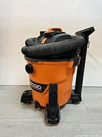 Front angled view of RIDGID wet/dry vacuum showing hose coiled on top, black feet base, and RIDGID logo front center