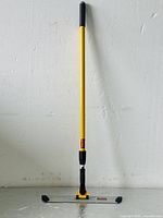 Full view of yellow Rubbermaid Commercial Pulse floor mop with handle and cleaning head, showing entire length and slim design.