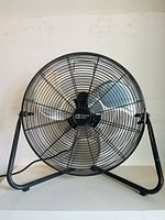 Front view of the black metal industrial fan showing metal cage and three silver metal blades.