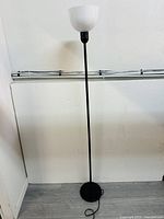 Full view of the standing floor lamp showing a tall slim black pole, round black base, and white bowl-shaped lamp shade.