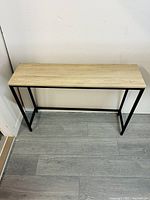 Rectangular wooden table with natural wood finish top and black metal legs shown from front view, demonstrating the table's design and condition.
