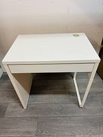 Full front and top view of white study table showing the drawer and cup holder on top, minor wear visible on back panel.