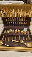 Full view of gold-toned Dirilyte flatware set in original box, showing knives on upright slots and spoons and forks in front compartments.