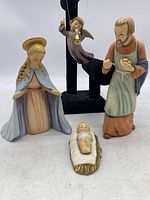 Group photo of four Goebel Hummel nativity figurines including Baby Jesus, Mary, Joseph, and Angel on a white background with partial black display stand visible behind.