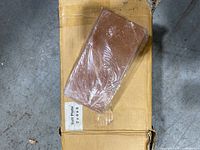 A Himalayan salt plate brick wrapped in plastic resting on top of the cardboard box labeled 'Salt Plate 2x4x8'.