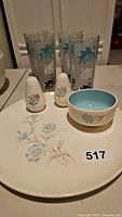 Four glasses, a small bowl, a large serving plate, and salt and pepper shakers all with floral and leaf designs in turquoise and black.