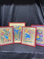 Four framed colorful Mexican folk art paintings on bark paper, showing bird and floral motifs in bright colors, set against a black fabric background.