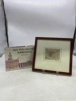 Overall view of both items, the framed map and the book side by side against a plain background.