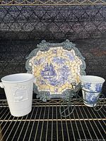 Photo showcasing mosaic wall hanging along with both pots and metal tricycle planter holder on a black metal shelf.