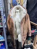 Front view of brown suede jacket open showing white shearling lining inside and attached hood.