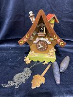 Front view of the wooden Disney-themed cuckoo clock with Mickey and Minnie figurines and pine cone weights laid in front.
