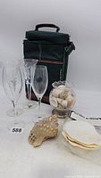 Photo of lot showing insulated wine carrier, two Dom Perignon wine glasses, two Waterford wine glasses, glass bowl with sea shells, large conical sea shell, and white sea shells.