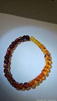Bracelet composed of rounded amber beads with a clear gradient from dark amber red to bright yellow amber beads, laid flat on a white surface.
