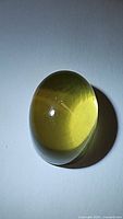 Photo of large oval cabochon citrine gemstone showing yellow golden color and smooth polished surface, photographed with reflective light to show translucency and internal clarity.