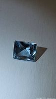 Close-up photo of a single rectangular aquamarine gemstone showing pale blue color and transparency with double-sided fancy cut facets.
