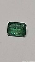Close-up of natural octagon cut emerald showing inclusions and coloration against a light background.