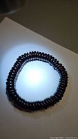 Single stretchy bracelet made of dark reddish-brown disk-shaped beads laid on flat surface under direct land light.