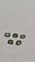 Five natural oval cut mint green sapphire gemstones shown together on a white background.