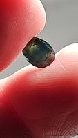 Close-up photo of a multicolored Ceylon sapphire held between fingers, showing blue, green, and yellow hues.