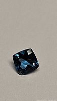 Close-up photo of a square cushion-cut natural London blue topaz gemstone with rich deep blue color and excellent clarity.