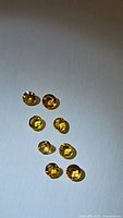 Nine round cut yellow sapphires scattered on light background showing size and color.