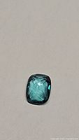 Close-up photo of a cushion-cut aqua blue topaz gemstone on a neutral background showing its color and cut.