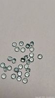 Multiple loose small round cut natural blue topaz gemstones approximately 2.5mm diameter laid out on plain background. Light to medium blue transparent stones with good VS clarity visible.