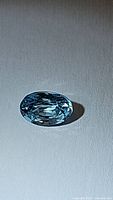 Oval cut lagoon blue Cambodian zircon gemstone photographed on a plain background, showing the top facet and clarity.