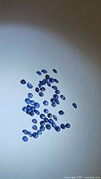 Photo shows multiple small round faceted Ceylon blue sapphires scattered on a white surface, showing their cornflower blue color and clarity.